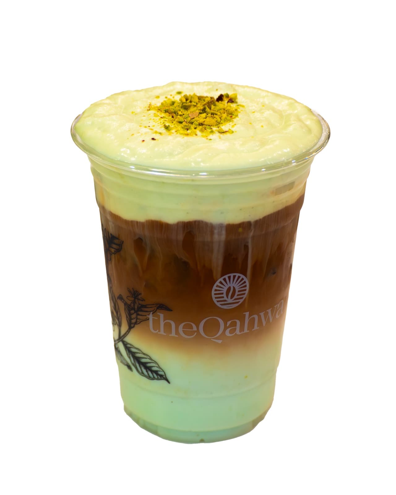Pistachio Cheesecake Latte in a clear theQahwa cup — espresso and milk over ice under a thick cheesecake-cream foam, finished with crushed pistachio.